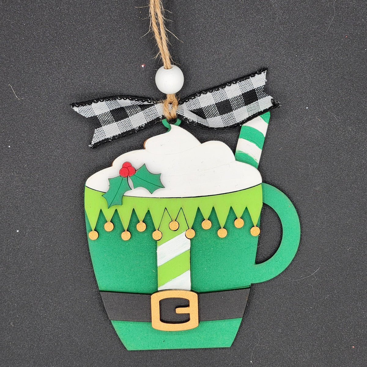 A DIY ornament shaped like a mug with cocoa and painted like an elf outfit.