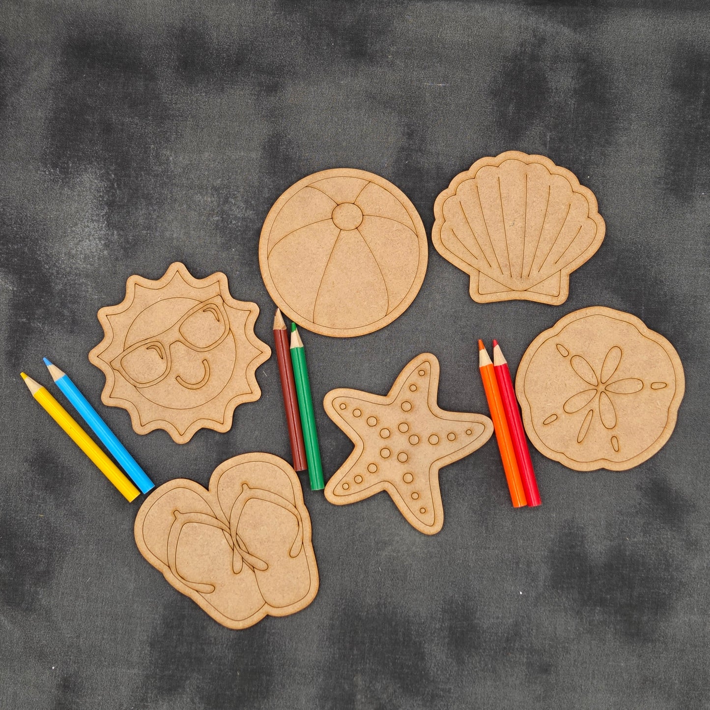 Set of wooden beach-themed shapes with colored pencils on a dark fabric background