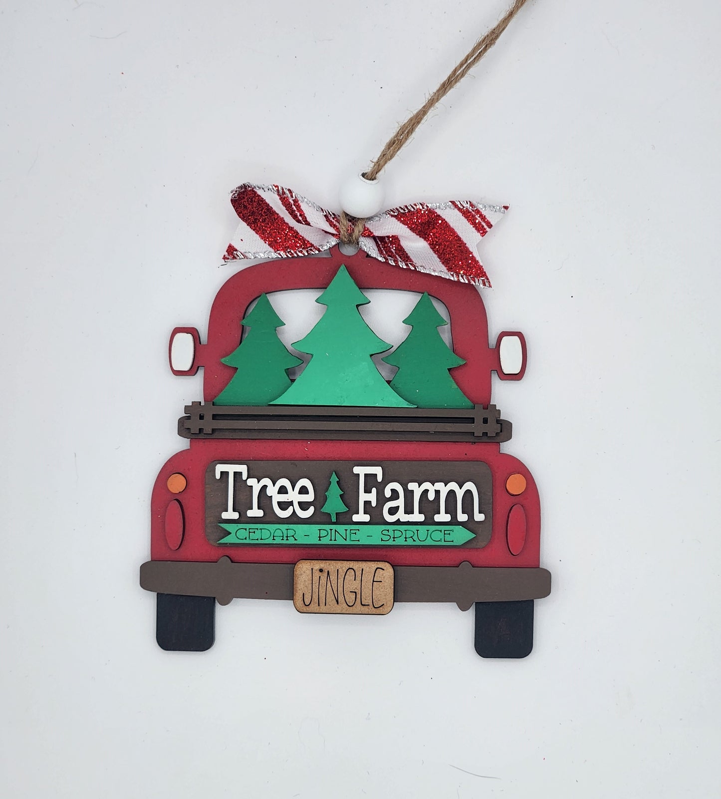 A craft kit to make a decorative truck ornament with a 'Tree Farm' and 'JINGLE' sign, featuring red and green colors and a Christmas tree in the bed of the truck.