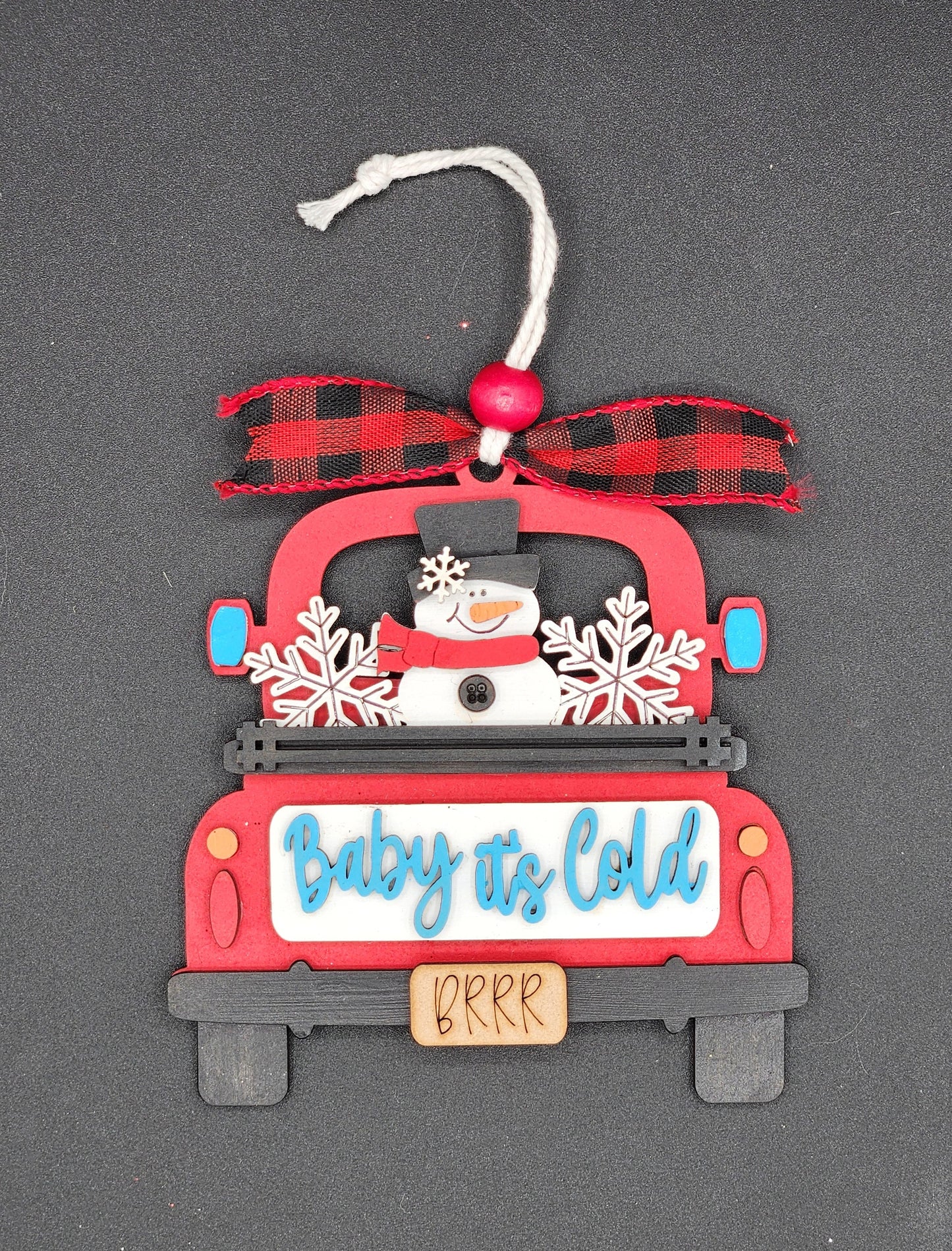 A red truck ornament with a bow, text 'Baby It's Cold', and snowflake patterns.