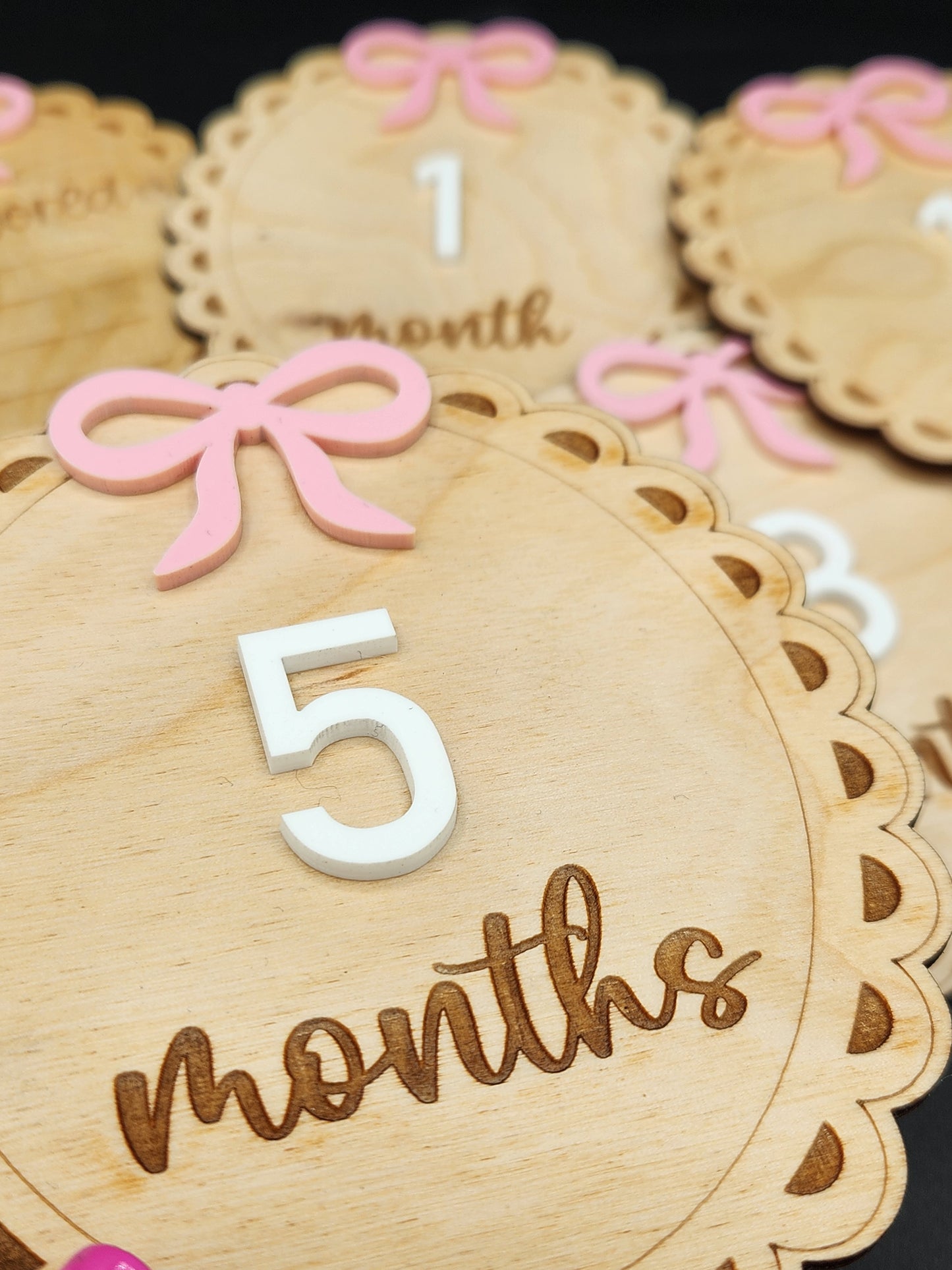 A collection of wooden milestones for baby's first year with engraved details, pink bows, and white numbers.