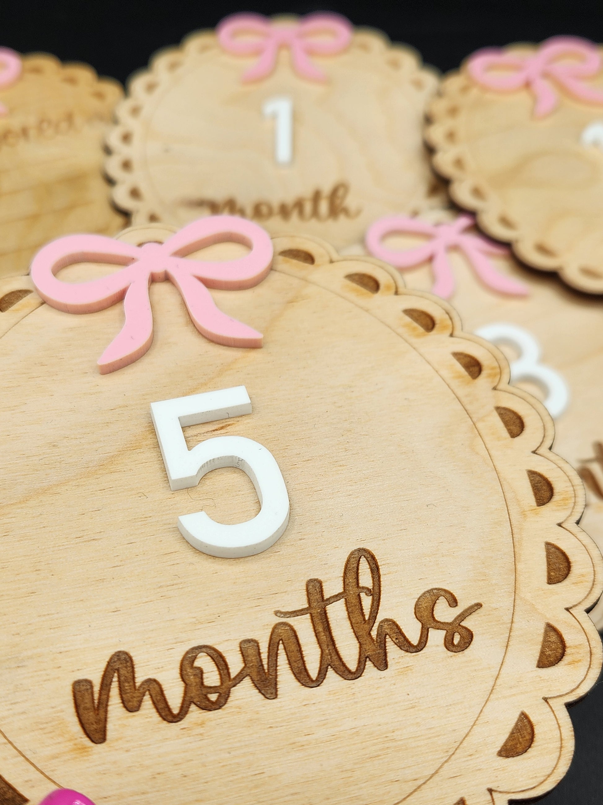A collection of wooden milestones for baby's first year with engraved details, pink bows, and white numbers.