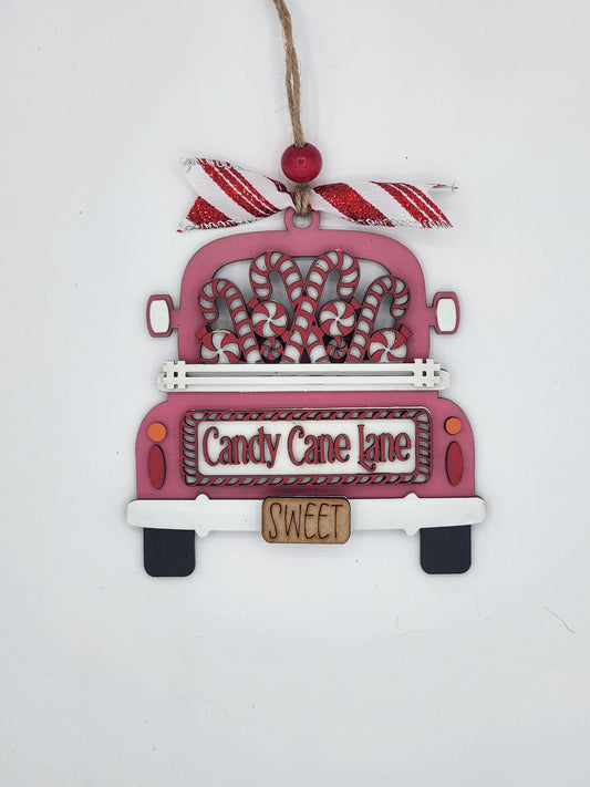 A DIY truck ornament kit with a candy cane lane design, including a pink truck with white and red accents, and decorative details.