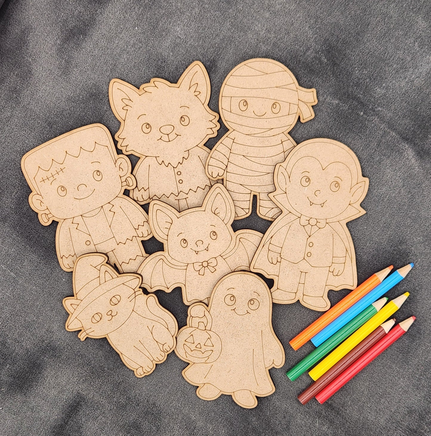 Wooden cutouts of Halloween characters with colored pencils on a gray surface