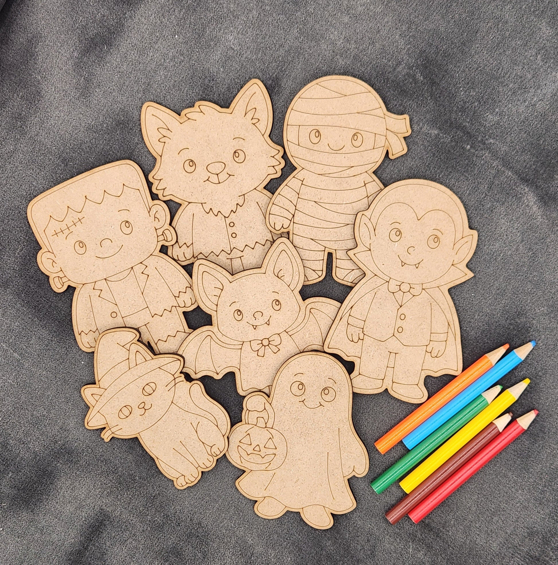 Wooden cutouts of Halloween characters with colored pencils on a gray surface