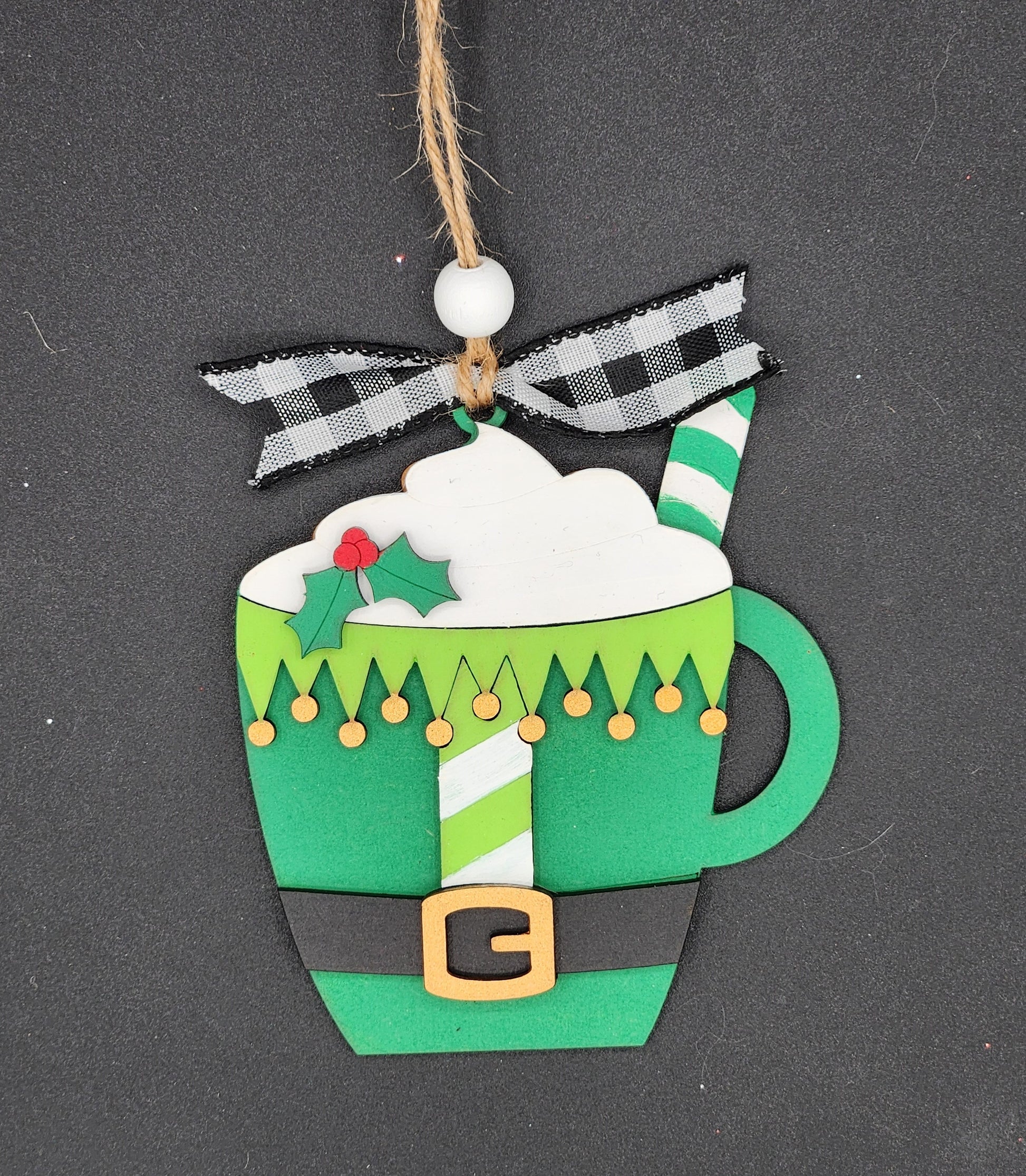 A DIY ornament shaped like a mug with cocoa and painted like an elf outfit.