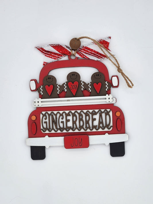 A red and white gingerbread man truck ornament with decorative details, hanging from a string.