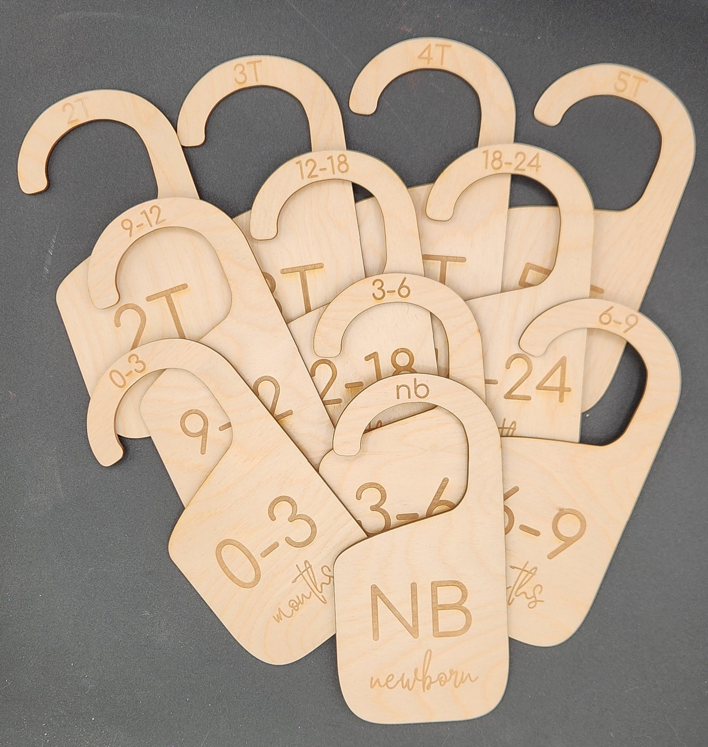 A collection of wooden hanger dividers for organizing baby clothing, each labeled with a different size range and age, displayed on a dark surface.