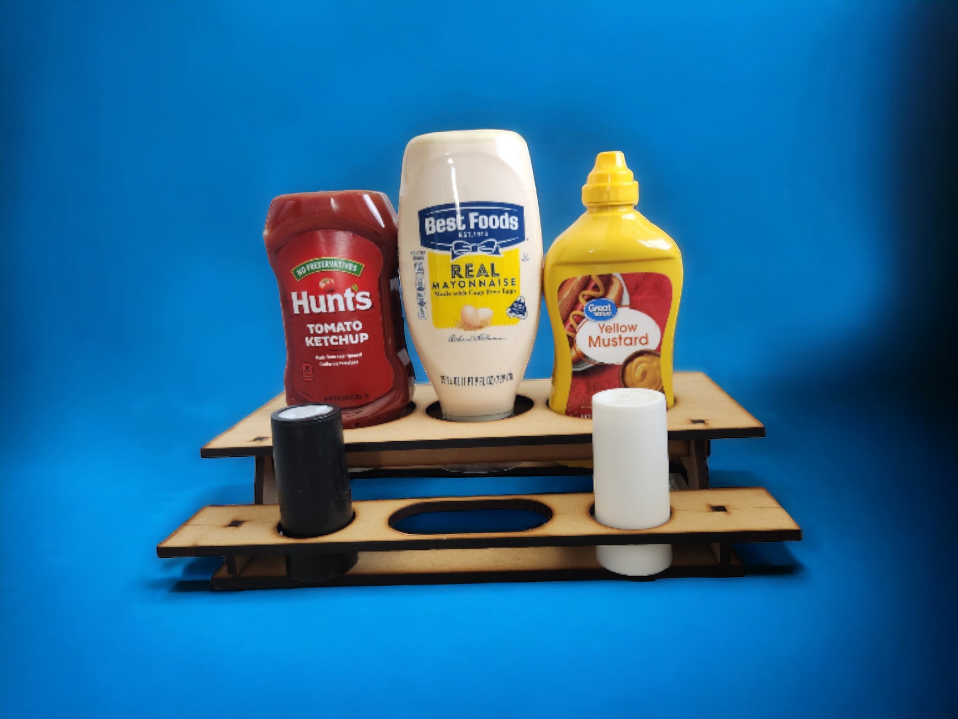 A wooden picnic table condiment holder with slots for ketchup, mustard, and mayonnaise bottles, displayed with the condiments arranged on it.