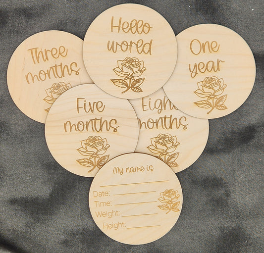 Wooden discs with engraved text and floral designs on a gray fabric background