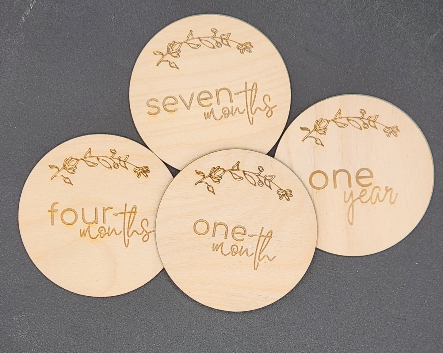 A set of wooden discs with 'one month', 'four months', 'seven months', and 'one year' printed on them, each surrounded by a floral pattern.
