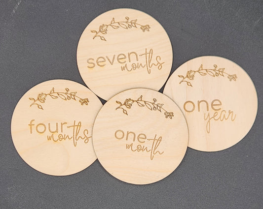 A set of wooden discs with 'one month', 'four months', 'seven months', and 'one year' printed on them, each surrounded by a floral pattern.